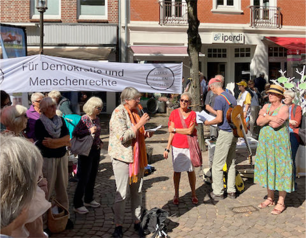 Menschen auf dem Rondeel, im Hintergrund das Transparent "Für Demokratie und Menschenrechte"