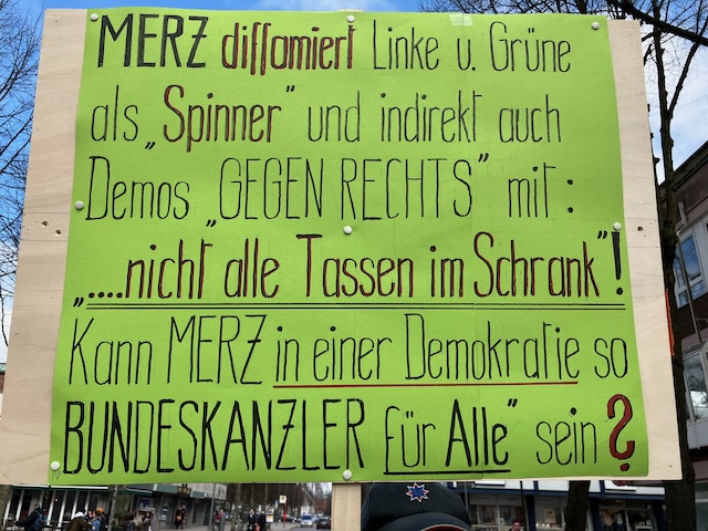 Schild mit Text: Merz diffamiert Linke u. Grüne als Spinner und indirekt auch die Demos GEGEN RECHTS mit ...nicht alle Tassen im Schrank. Kann Merz in einer Demokratie so Bundeskanzler für alle sein?